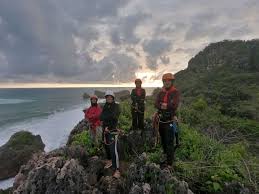 Gambar Pantai Siung dengan tebing batu tinggi dan orang sedang memanjat.