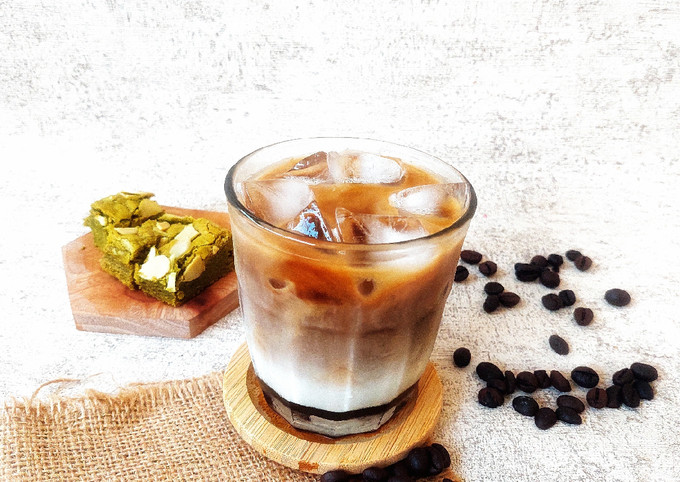 Gelas es kopi susu gula aren dengan latte art dan es batu di meja kafe.