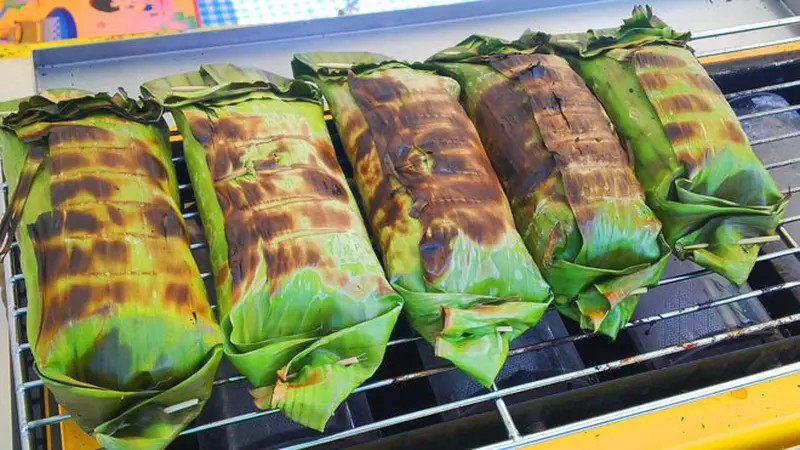 Nasi bakar dengan lauk ayam suwir di atas daun pisang yang dibakar.
