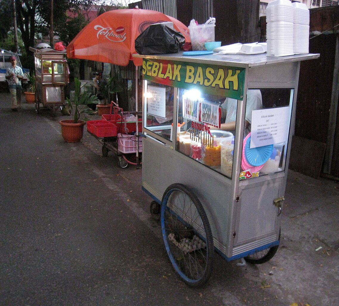 Gerobak seblak dengan antrean pembeli dan asap mengepul di pinggir jalan.
