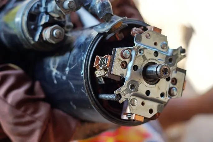 Teknisi sedang memperbaiki dinamo starter mobil di meja kerja bengkel.