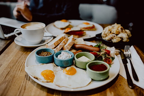 Piring brunch dengan scrambled egg, sosis, roti panggang, dan salad di meja kafe.