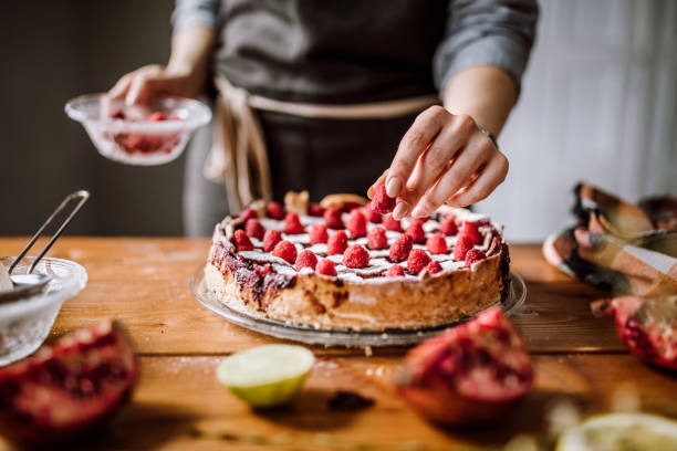 Chef patissier sedang menghias kue dengan krim dan buah-buahan di sebuah workshop baking.