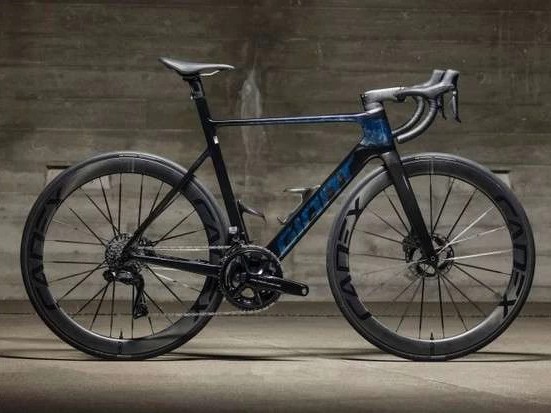 Gambar sepeda jalan Giant Propel dalam pose balap dinamis di jalan aspal yang bersih, dengan latar belakang buram yang mengisyaratkan kecepatan, dan sedikit latar belakang kota Surabaya.