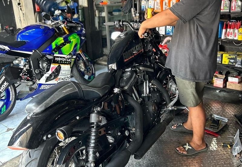 Motor Gede (Moge) berwarna hitam glossy sedang diservis di bengkel spesialis dengan peralatan khusus.