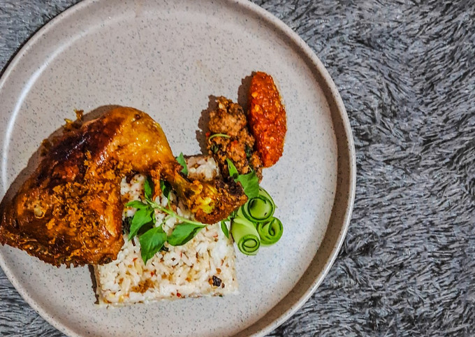 Nasi tutug oncom dengan ayam goreng, tempe, dan sambal di piring.