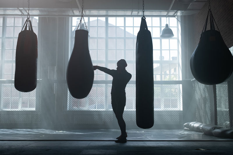 Orang sedang berlatih boxing atau Muay Thai di ring atau dengan samsak, suasana intens dan bersemangat.