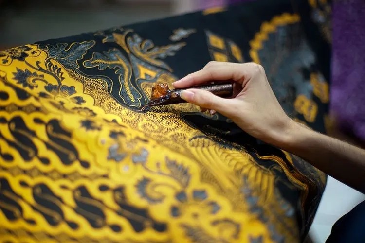 Tangan sedang mencanting batik di sebuah workshop batik tradisional.