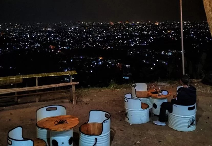 Pasangan duduk di kafe rooftop dengan pemandangan city light Bandung di malam hari.