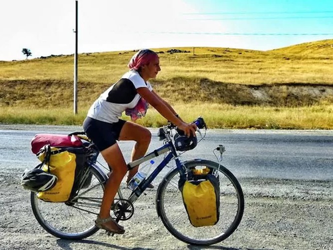 Gambar sepeda touring Thorn Nomad terisi penuh dengan tas bikepacking, di jalan jarak jauh yang indah dengan pegunungan di latar belakang, menonjolkan kesiapan petualangannya, dengan latar belakang sa