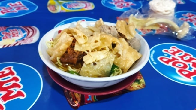 Semangkuk mie ayam bakso hangat disajikan di meja warung kaki lima di malam hari.