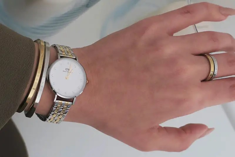 Pergelangan tangan wanita dengan jam tangan elegan dan gelang tipis, menunjukkan detail dial yang feminin.