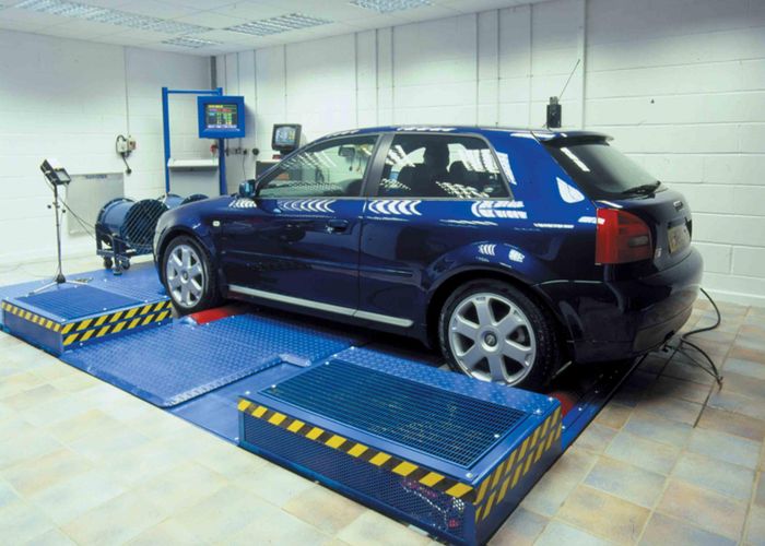 Mobil sedang di atas mesin dyno test, dengan mekanik memantau data di komputer.