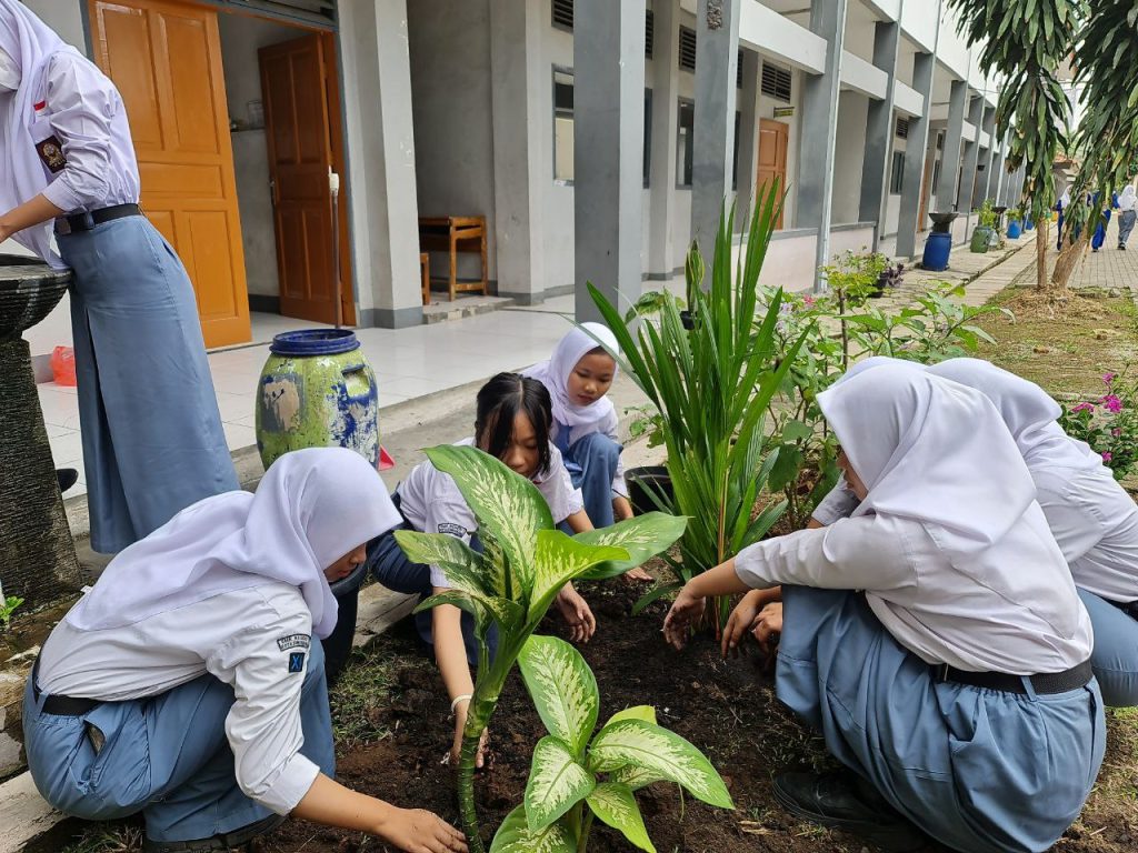 Gambar siswa-siswi menanam bibit pohon di kebun sekolah yang asri.