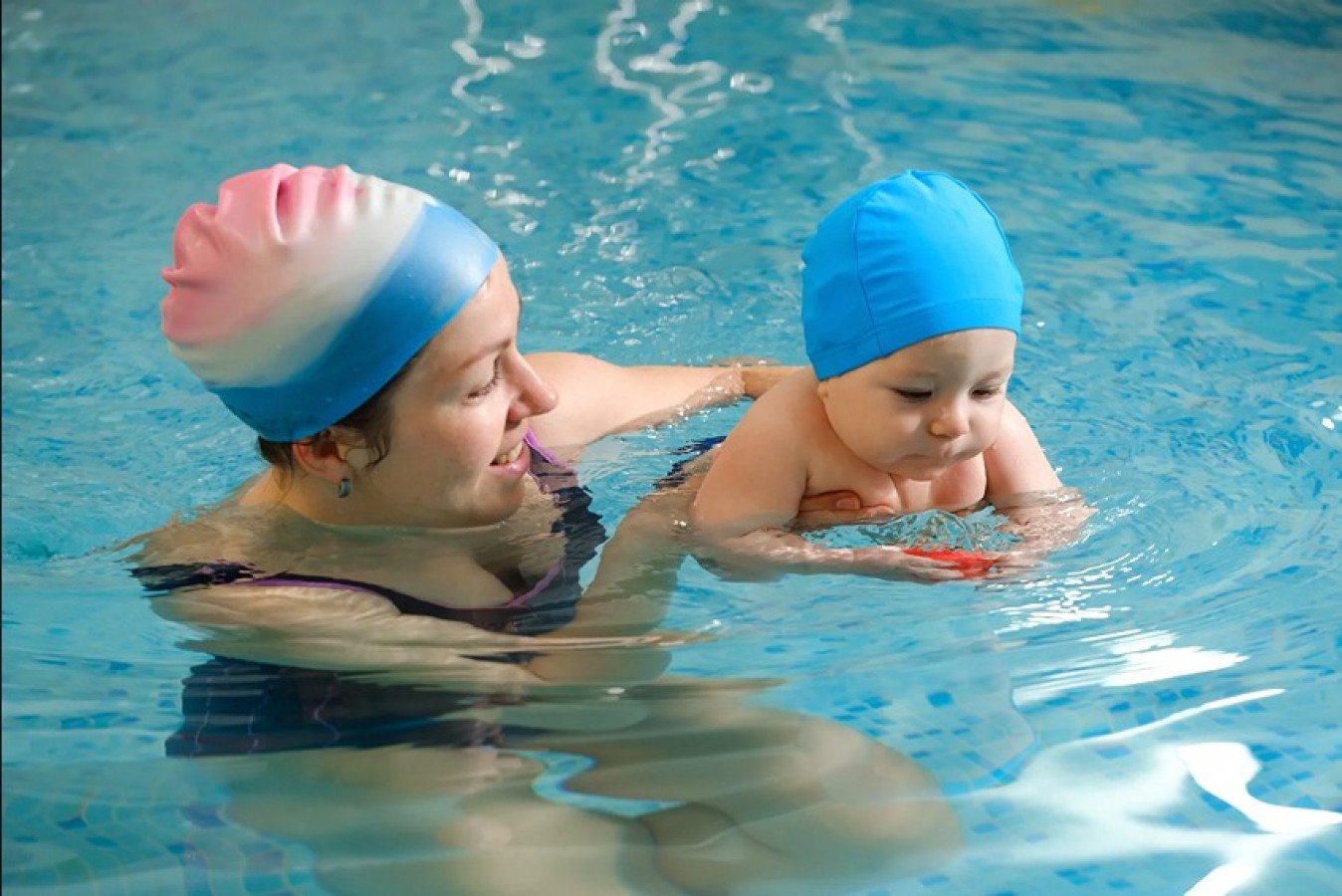 Bayi sedang diajari berenang oleh orang tuanya di kolam renang yang dangkal dan hangat.