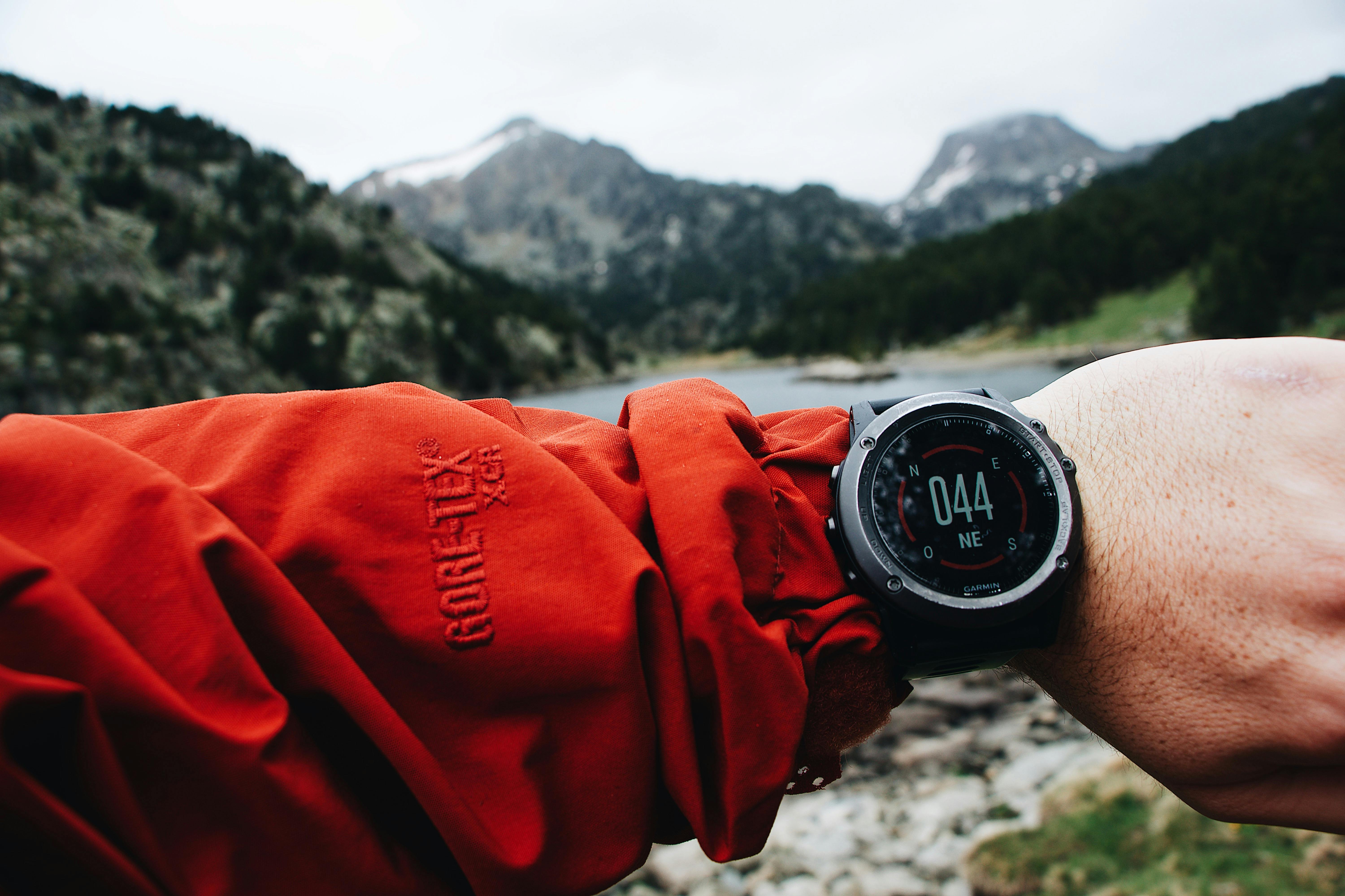 Jam tangan outdoor tangguh di pergelangan tangan, dengan latar belakang gunung atau hutan.