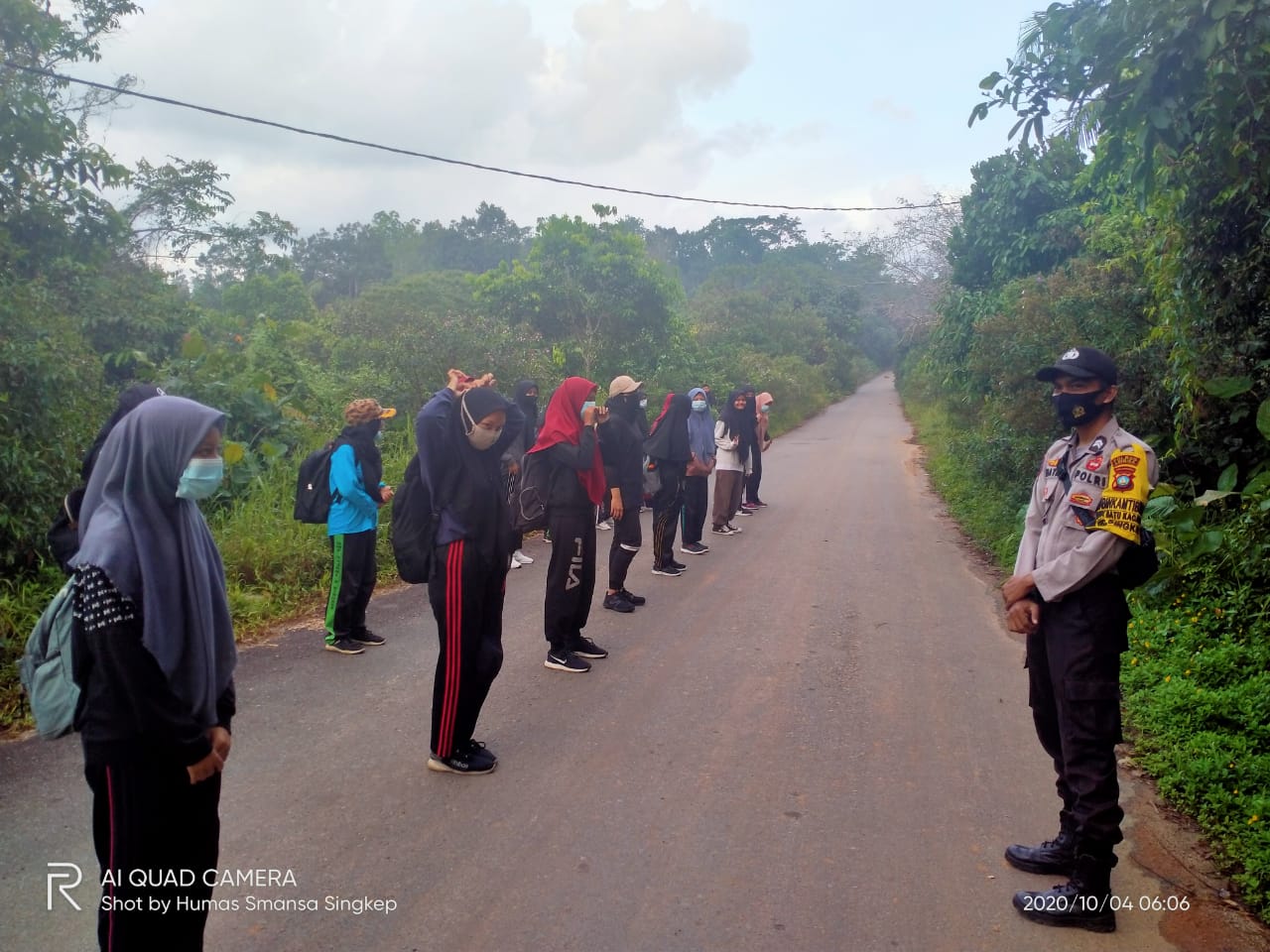 Gambar siswa-siswi sedang melakukan kegiatan hiking di jalur alam, mengenakan backpack dan topi.