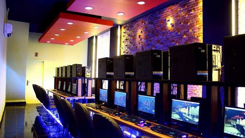 Bagian dalam warnet yang terang di malam hari, menunjukkan beberapa orang masih fokus di depan komputer.