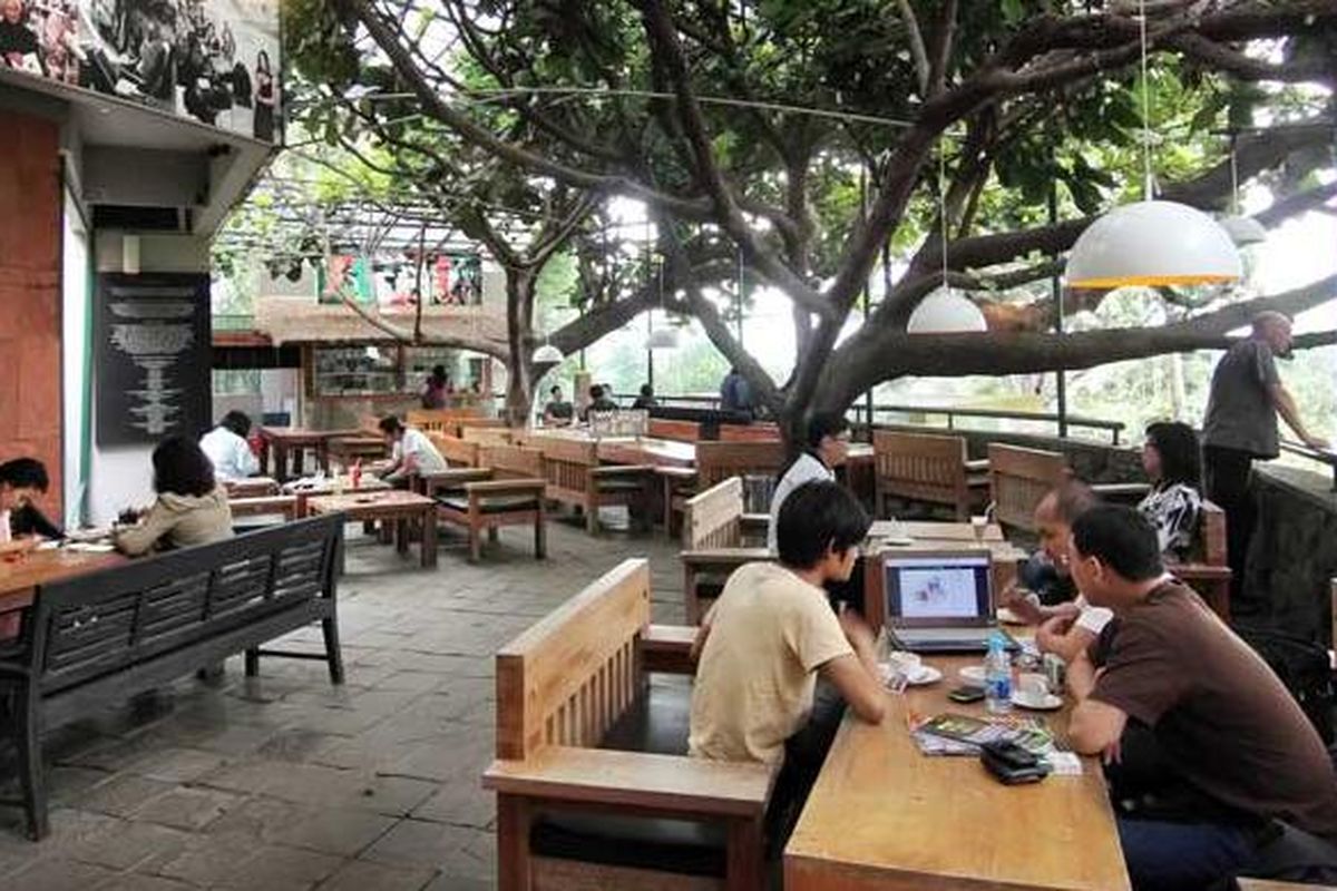 Interior kedai kopi modern dengan suasana ramai anak muda yang sedang nongkrong dan minum kopi.