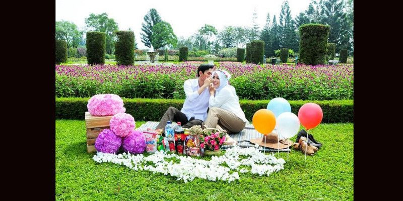 Keluarga sedang piknik di taman bunga yang indah dengan latar belakang bunga berwarna-warni.