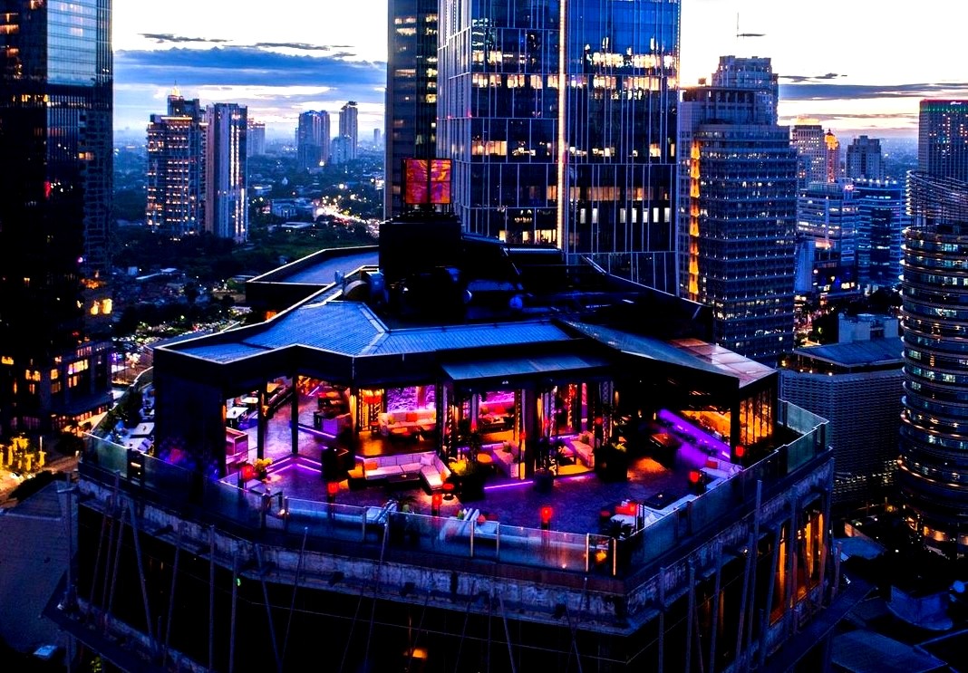 Pemandangan kota Jakarta di malam hari dari sebuah rooftop bar mewah.