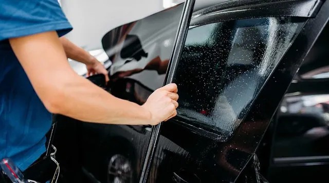 Teknisi sedang memasang kaca film pada jendela mobil di sebuah bengkel.