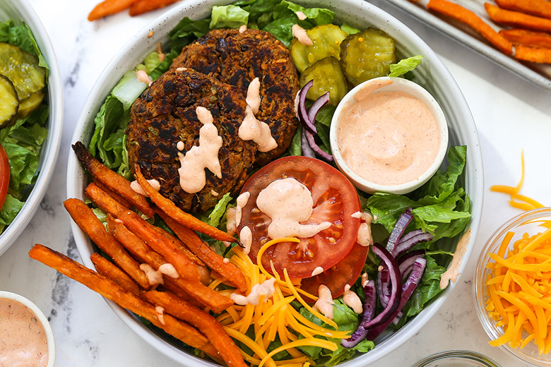 Piring berisi plant-based burger dengan sayuran segar dan ubi goreng.