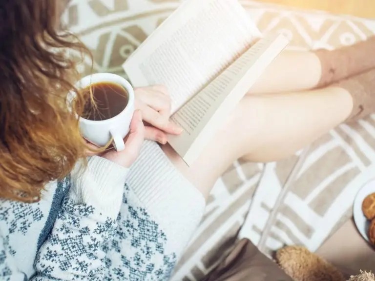 Seseorang sedang membaca buku di meja cafe yang tenang dengan segelas kopi.