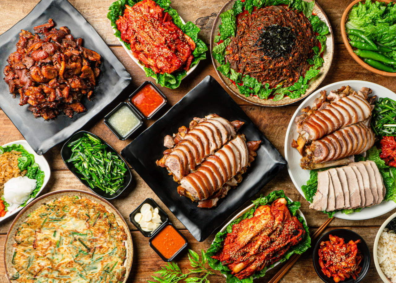 Meja restoran dengan berbagai hidangan Korean BBQ, ssamjang, kimchi, dan side dish Korea.