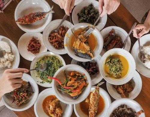Piring berisi rendang daging dan berbagai lauk pauk masakan Padang di meja restoran.