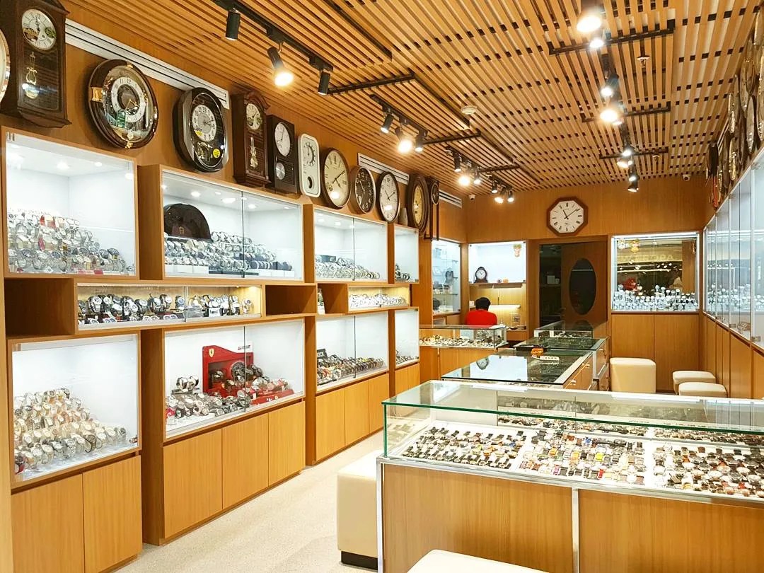 Gambar toko jam tangan yang cerah dan modern, menampilkan berbagai macam jam tangan fashion di rak dan etalase kaca.