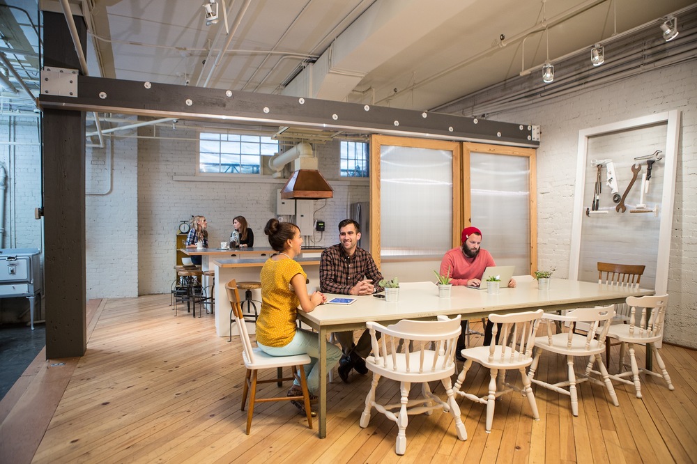 Interior co-working space CoHive Dago dengan orang-orang sedang bekerja di meja komunal.