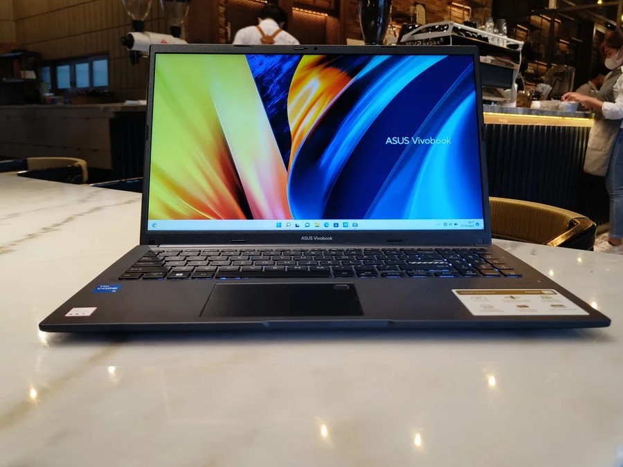 Gambar ASUS VivoBook 15 di meja di kantor rumah atau kamar siswa, menyoroti desain fungsionalnya, mungkin dengan latar belakang WTC Surabaya.