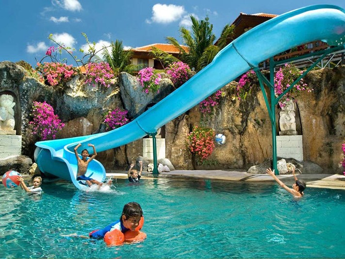 Gambar kolam renang hotel dengan seluncuran air kecil dan anak-anak bermain.