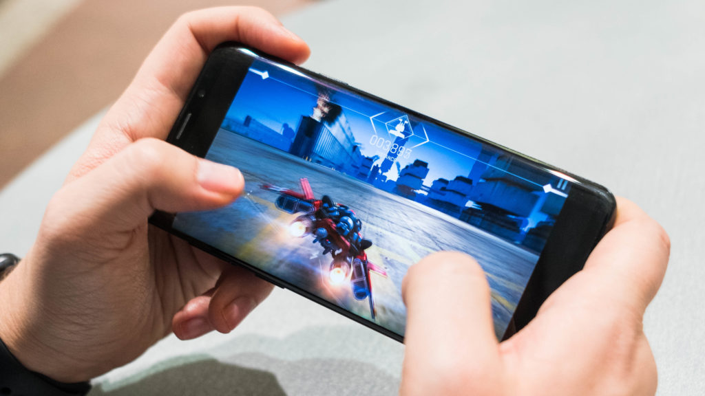 Tangan sedang memegang ponsel gaming yang menampilkan efek getaran di layar saat bermain game.