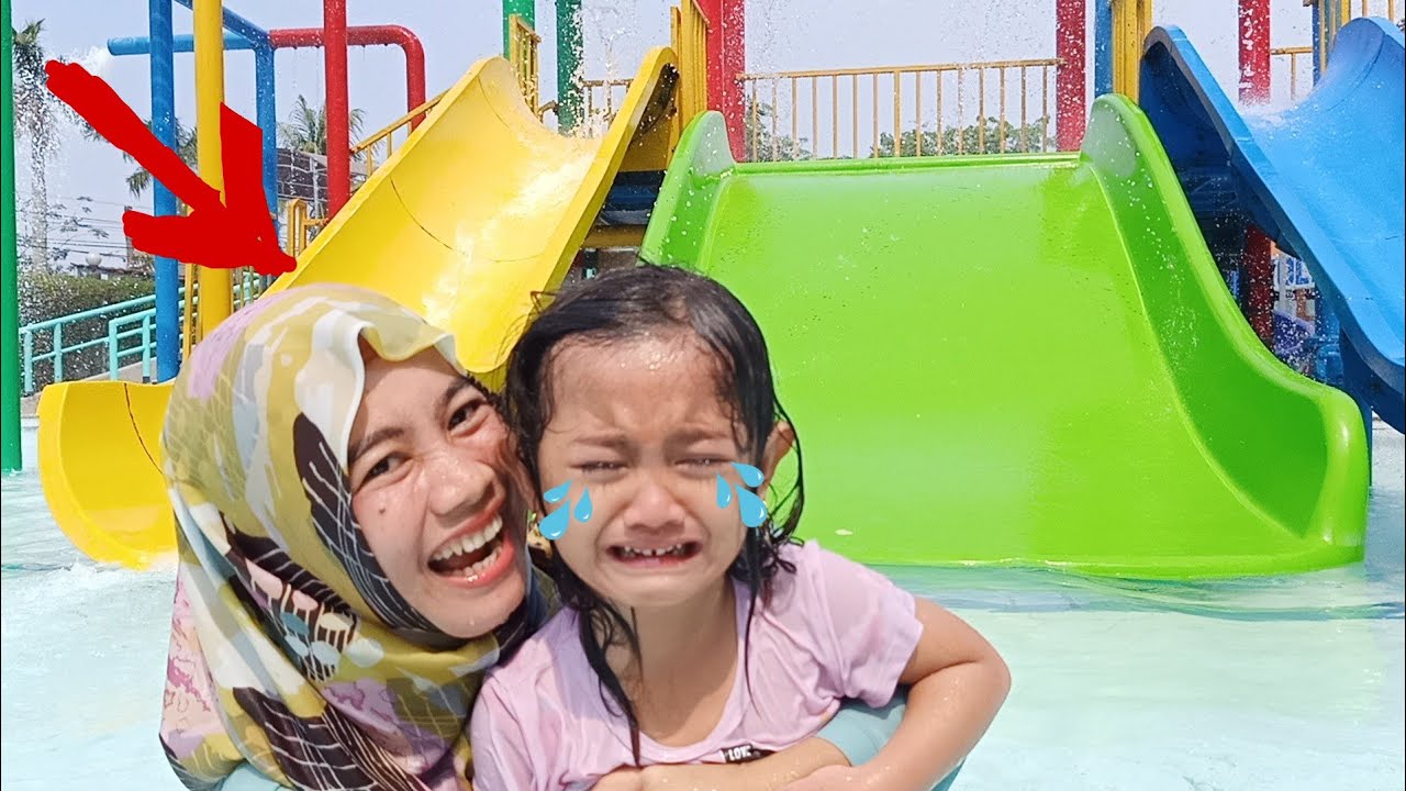 Anak-anak sedang bermain di kolam renang dangkal dengan perosotan air mini.