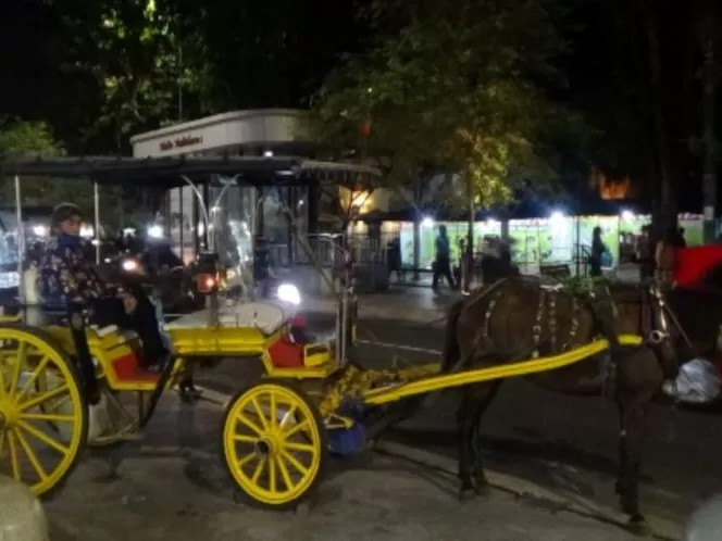 Gambar Jalan Malioboro di malam hari dengan pedagang kaki lima dan andong.