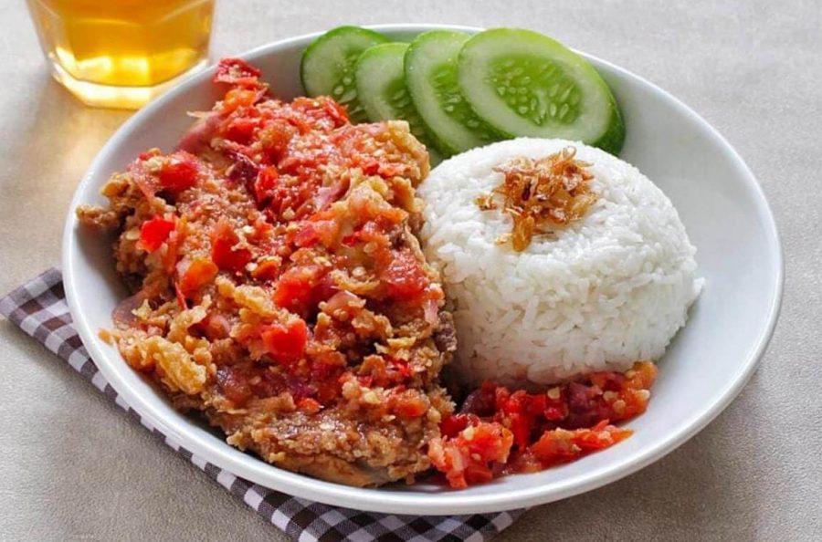 Ayam geprek dengan sambal berwarna merah yang terlihat sedikit mengkilap, disajikan di atas nasi.