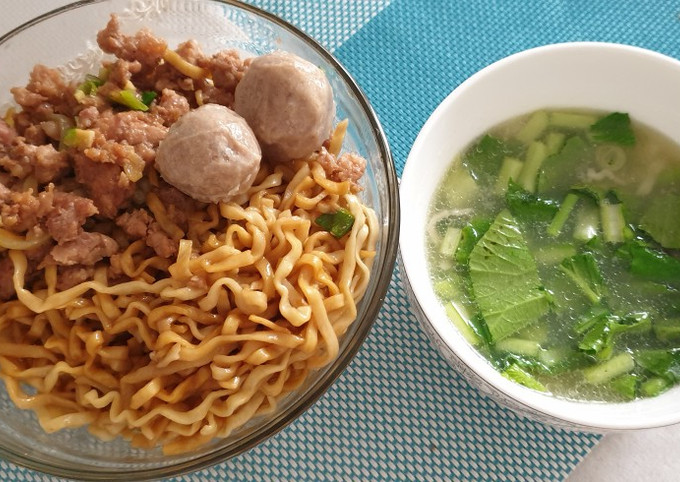 Semangkuk mie ayam dengan topping ayam cincang dan bakso, disajikan dengan kuah terpisah.