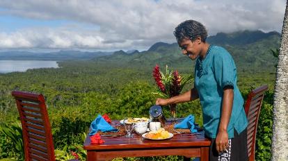 Keluarga menikmati hidangan di restoran outdoor area resort all-inclusive dengan pemandangan hijau.