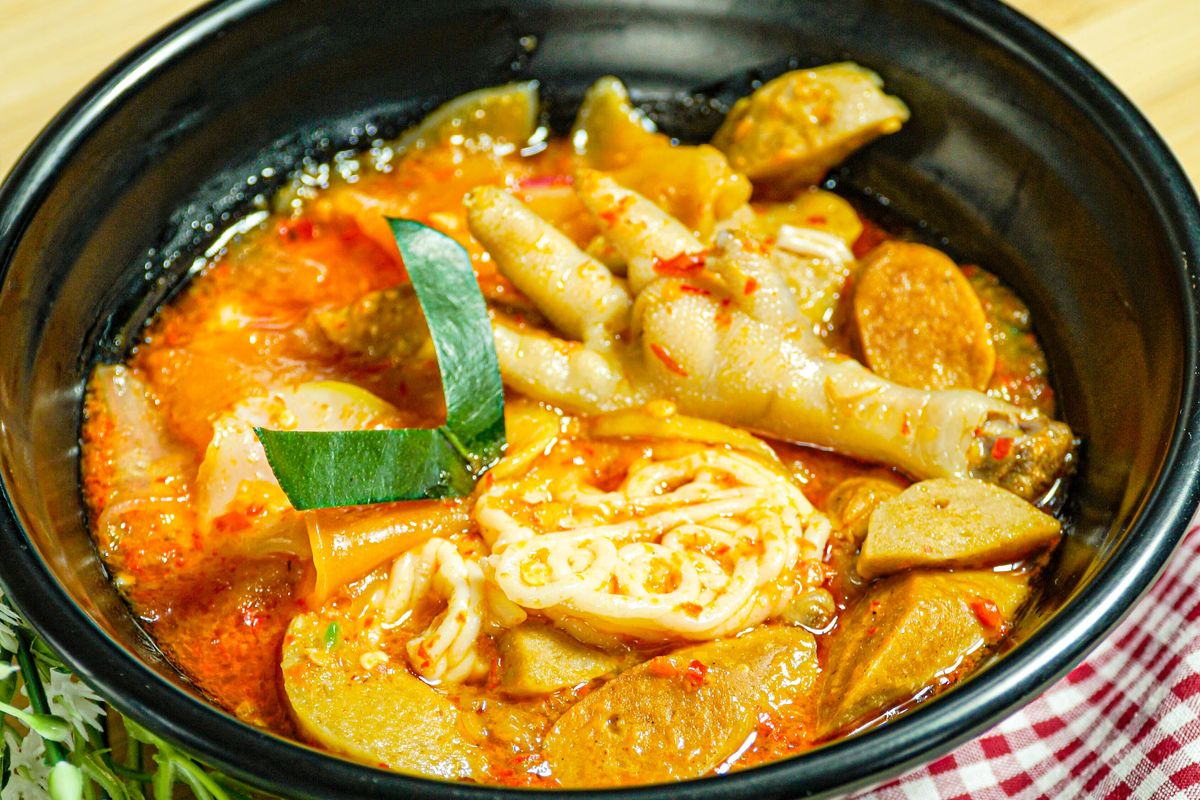 Semangkuk seblak pedas dengan kuah merah, kerupuk, dan topping ceker ayam.