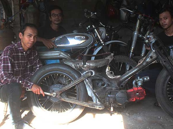 Gambar bengkel yang mengkhususkan diri pada motor klasik dan custom, dengan motor vintage dan proyek custom yang sedang berjalan.
