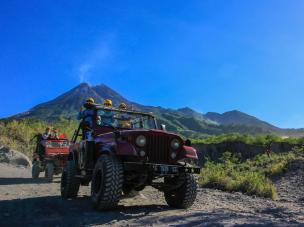 Gambar Jeep melaju di lanskap vulkanik dengan Gunung Merapi.