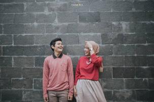 Seorang perempuan berfoto selfie di depan dinding estetik sebuah cafe dengan pencahayaan hangat.