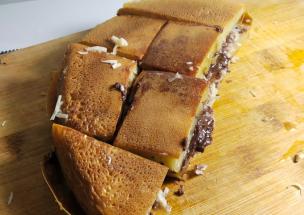 Potongan martabak manis dengan topping keju parut dan cokelat butiran yang melimpah.