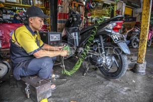Montir sedang memperbaiki motor di sebuah bengkel motor.