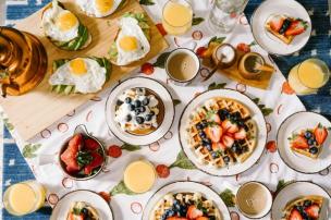 Meja penuh hidangan brunch klasik seperti eggs benedict, waffle, dan kopi.