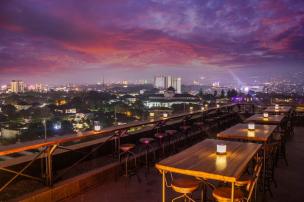 Pemandangan kafe rooftop di Bandung dengan langit senja berwarna jingga dan lampu kota mulai menyala.