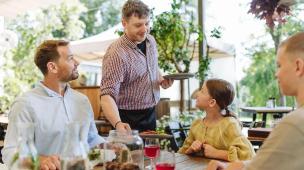 Keluarga makan bersama di restoran dengan anak-anak tersenyum.