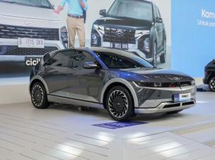 Gambar Hyundai Ioniq 5 abu-abu sedang mengisi daya di stasiun EV di lingkungan perkotaan, menonjolkan desain rampingnya, dengan latar belakang samar SCBD Jakarta Selatan.